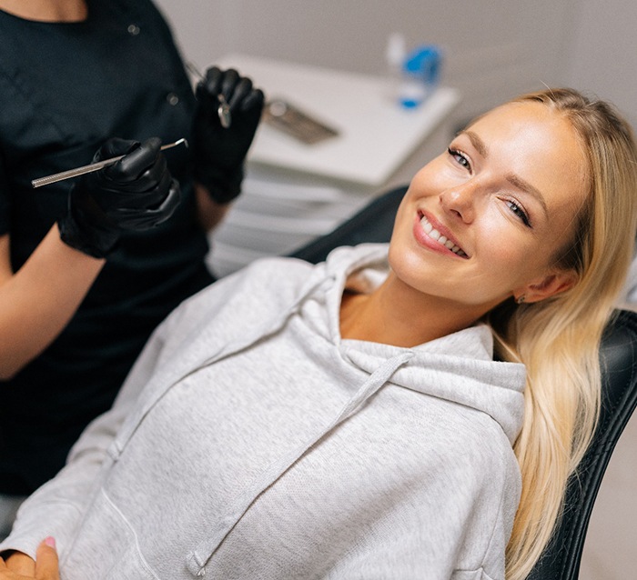 Woman in gray sweatshirt smiling while sitting in treatment chair