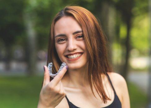 Smiling woman holding an Invisalign clear braces tray